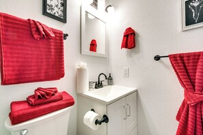 A bathroom with a white sink, a toilet, and a mirror. There are red towels hanging on the wall and a red robe on a hook.
