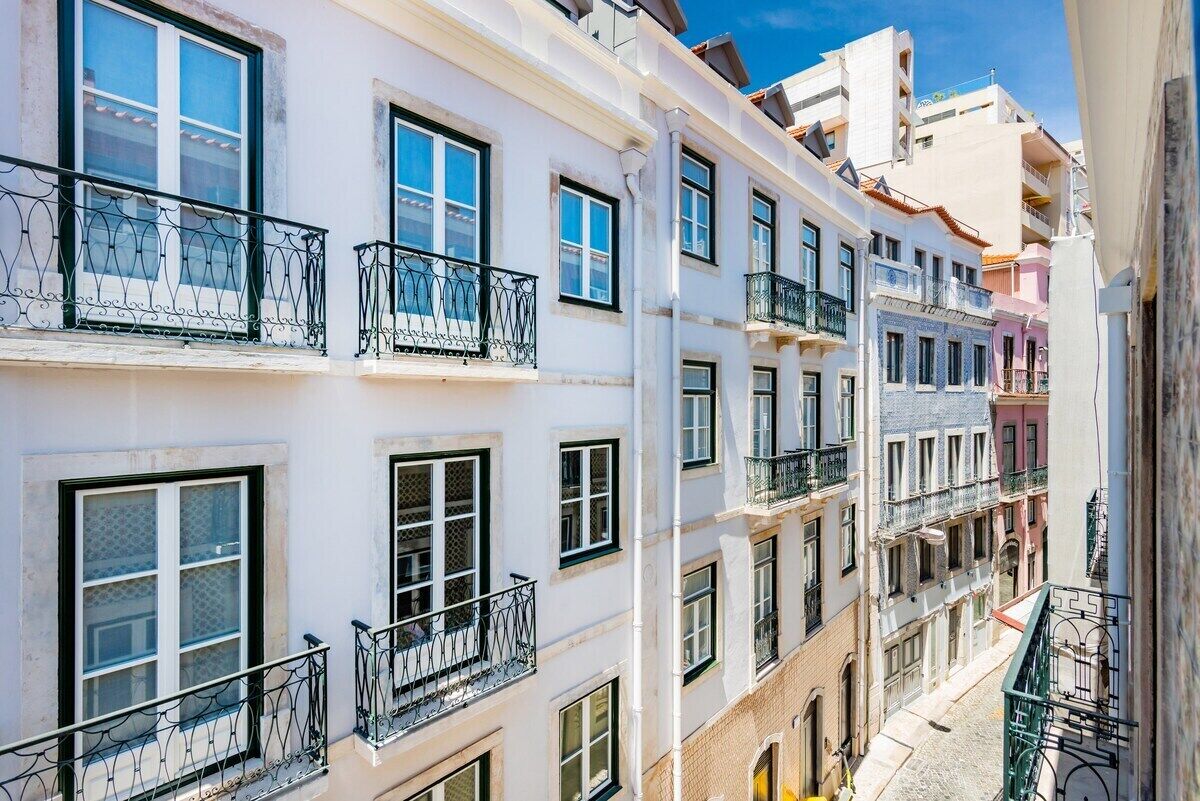 Un edificio de varios pisos con balcones, una calle estrecha y edificios colindantes.