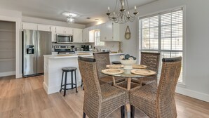 Een moderne keuken met een centraal eiland, roestvrijstalen apparatuur, rieten stoelen en een kroonluchter.