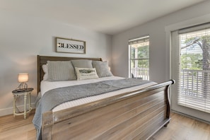 A bedroom with a wooden bed frame, a bedside table with a lamp, a framed sign on the wall, and a window with blinds. - Walkable 30A Getaway! Coastal Cottage & Suite (Santa Rosa Beach)