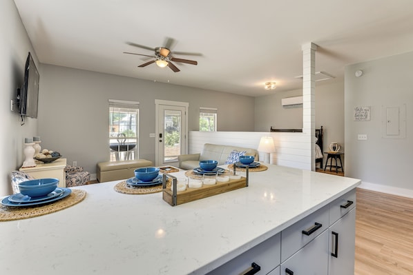 A modern kitchen with a marble countertop, a ceiling fan, and a dining area with a sofa and table. - Walkable 30A Getaway! Coastal Cottage & Suite (Santa Rosa Beach)