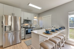 A modern kitchen with stainless steel appliances, a central island with stools, and a view of the outdoors. - Walkable 30A Getaway! Coastal Cottage & Suite (Santa Rosa Beach)