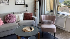A living room with a grey sofa, a round coffee table, a pink armchair, and a large window with a view. - 5 Star Holiday Home in Uddevalla (Uddevalla)