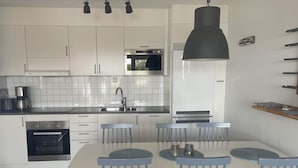 A modern kitchen with white cabinets, a built-in oven, a microwave, and a large black pendant light. - 5 Star Holiday Home in Uddevalla (Uddevalla)