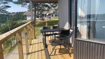 A wooden deck with outdoor furniture, a glass door, and a view of a residential area with houses and trees.
