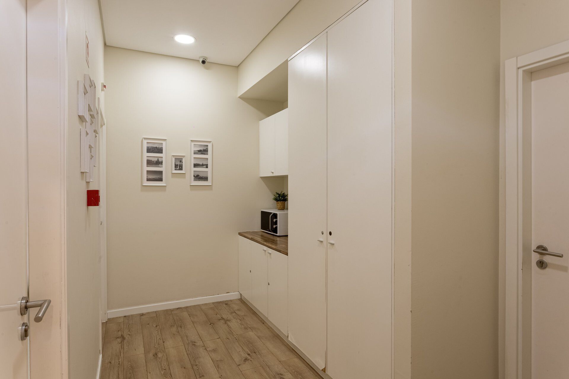 Un corridoio con pavimento in legno, pareti bianche, un forno a microonde su uno scaffale e una porta con una serratura rossa.