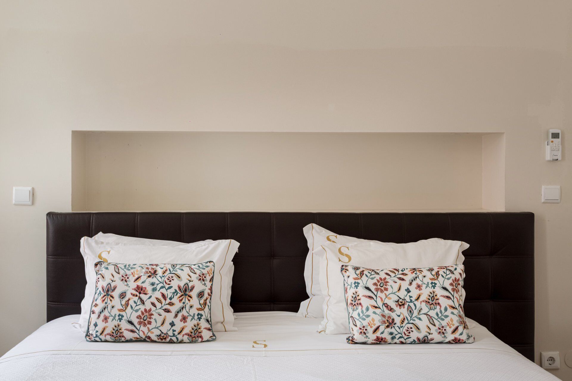 Un letto con una testiera scura, due cuscini floreali e una coperta bianca.