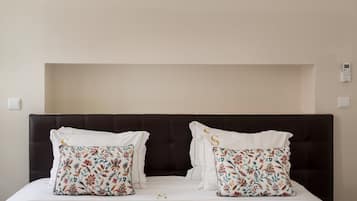 Un letto con una testiera scura, due cuscini floreali e una coperta bianca.