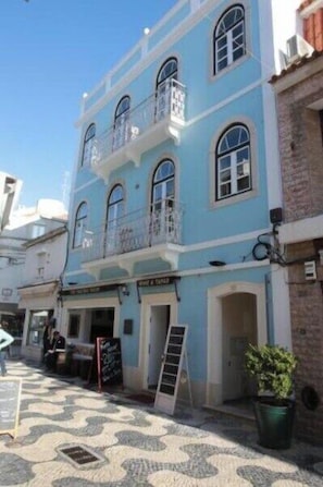 A two-story building with a balcony, a signboard, and a potted plant on the ground floor. - Superior Double Room @ Sui7es Guest House Cascais (Cascais)