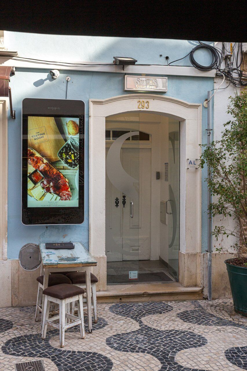 L’entrée d’un hôtel, avec une porte en verre, une enseigne au-dessus de la porte et un panneau d’affichage numérique fixé au mur.