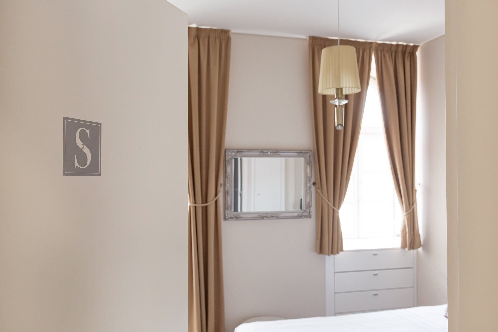 A bedroom with a bed, a dresser, a mirror, and curtains.