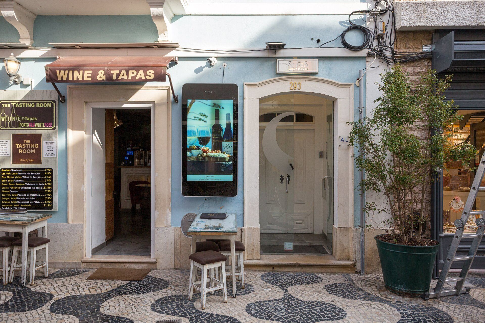 Un ristorante di vino e tapas con una lavagna dei menu, posti a sedere all'aperto e una porta con il numero 293.