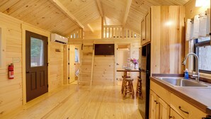 Ein Interieur einer Holzhütte mit Küchenbereich, Holzdielen und einem Deckenventilator.