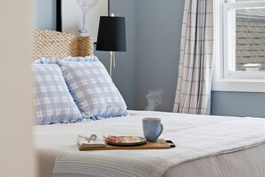 Una cama bien hecha con una almohada de cuadros, una taza y un plato con comida.