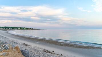 A beach with pebbles, a clear sky, and a calm sea.