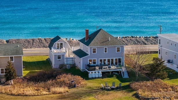 A coastal house with a large porch, a chimney, and a view of the ocean.