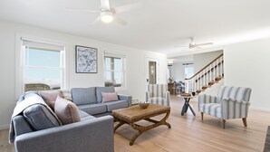A spacious living room with a grey sofa, a striped armchair, a woven coffee table, and a staircase leading to another level.