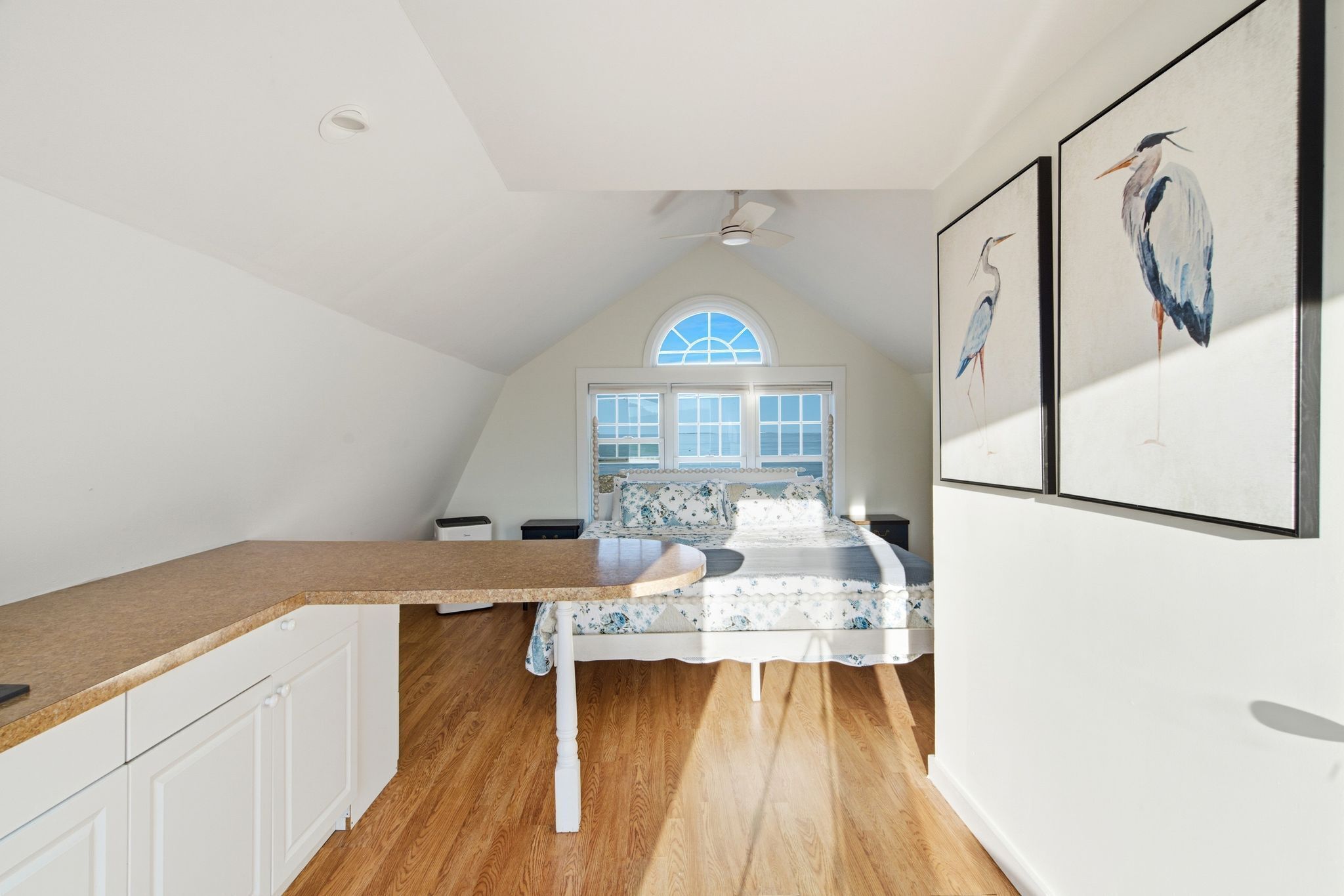 A bedroom with a bed, a window, a ceiling fan, and wall-mounted artwork.