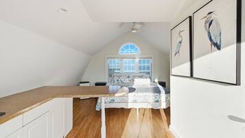 A bedroom with a bed, a window, a ceiling fan, and wall-mounted artwork.