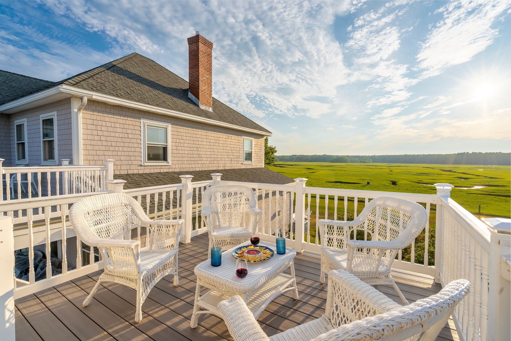 A deck with wicker chairs and a table, overlooking a green field.