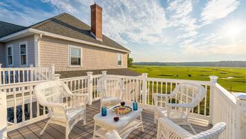 A deck with wicker chairs and a table, overlooking a green field.