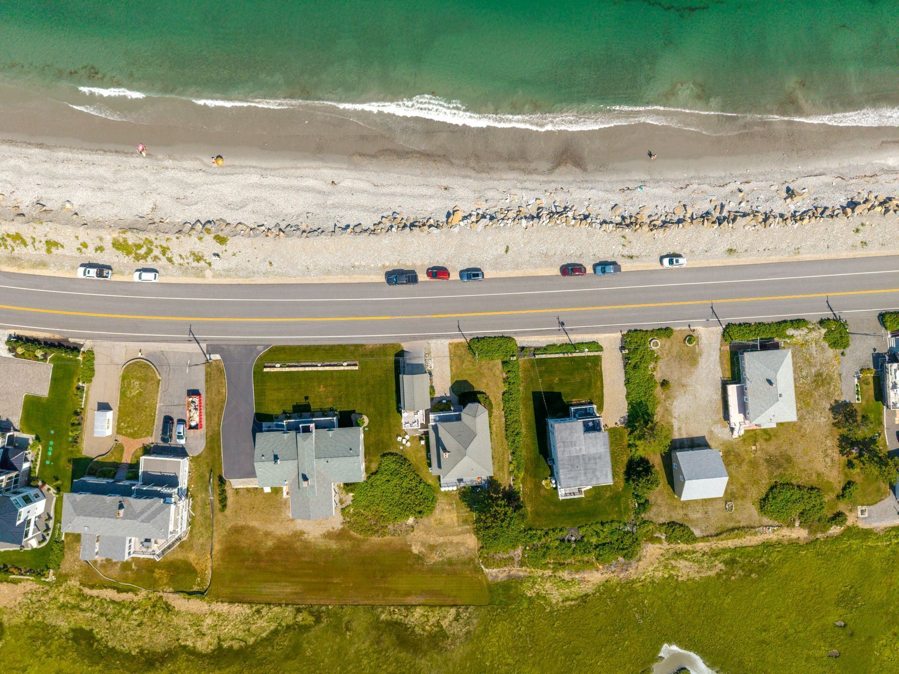 An aerial view of a coastal residential area with houses, a road, and a beach.