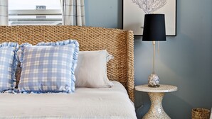 A bed with a woven headboard, a round table with a mosaic base, and a framed artwork on the wall.
