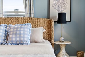 A bed with a woven headboard, a round table with a mosaic base, and a framed artwork on the wall.