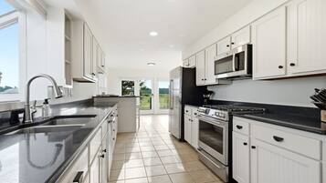 A modern kitchen with white cabinets, a black countertop, stainless steel appliances, and a view to the outdoors.