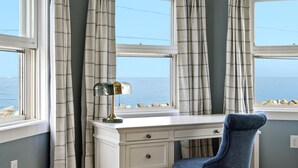 A room with a desk, chair, and large windows with curtains.