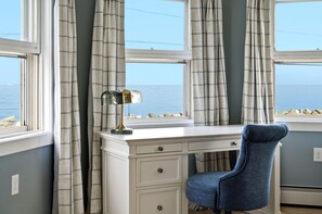 A room with a desk, chair, and large windows with curtains.