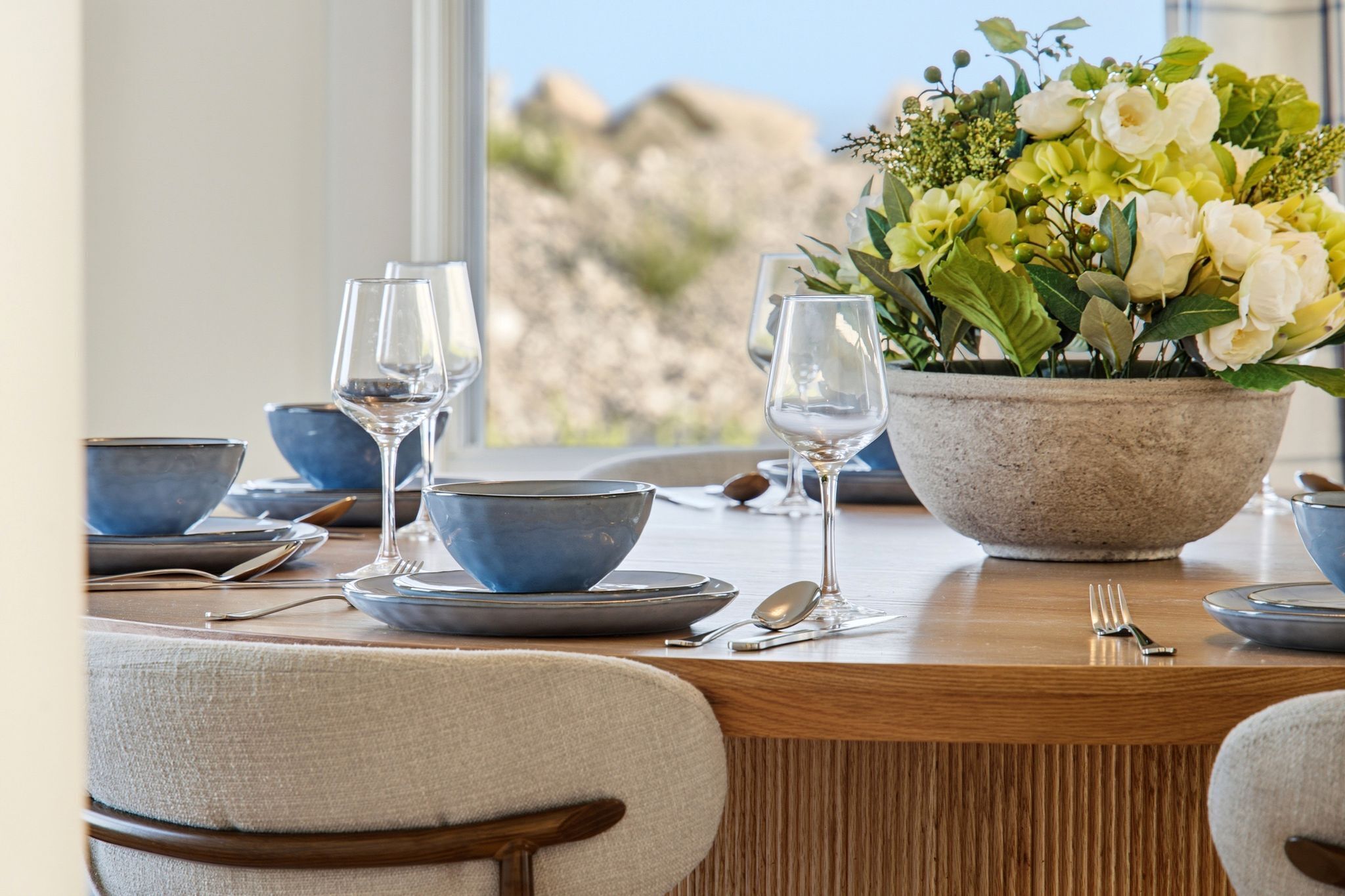 A dining table set with blue bowls, plates, and wine glasses, accompanied by a centerpiece of flowers.
