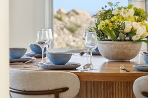 Una mesa de comedor dispuesta con cuencos, platos y copas de vino, adornada con un centro de flores.