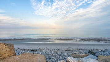 A beach with pebbles and rocks in the foreground, a calm sea, and a clear sky with clouds.
