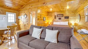Een gezellig blokhut interieur met houten plafond, een bank, een bed en een eethoek.
