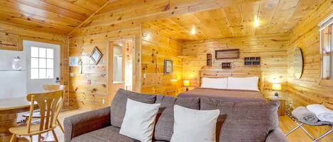 Un interior de cabaña acogedor con techo de madera, un sofá, una cama y un comedor.