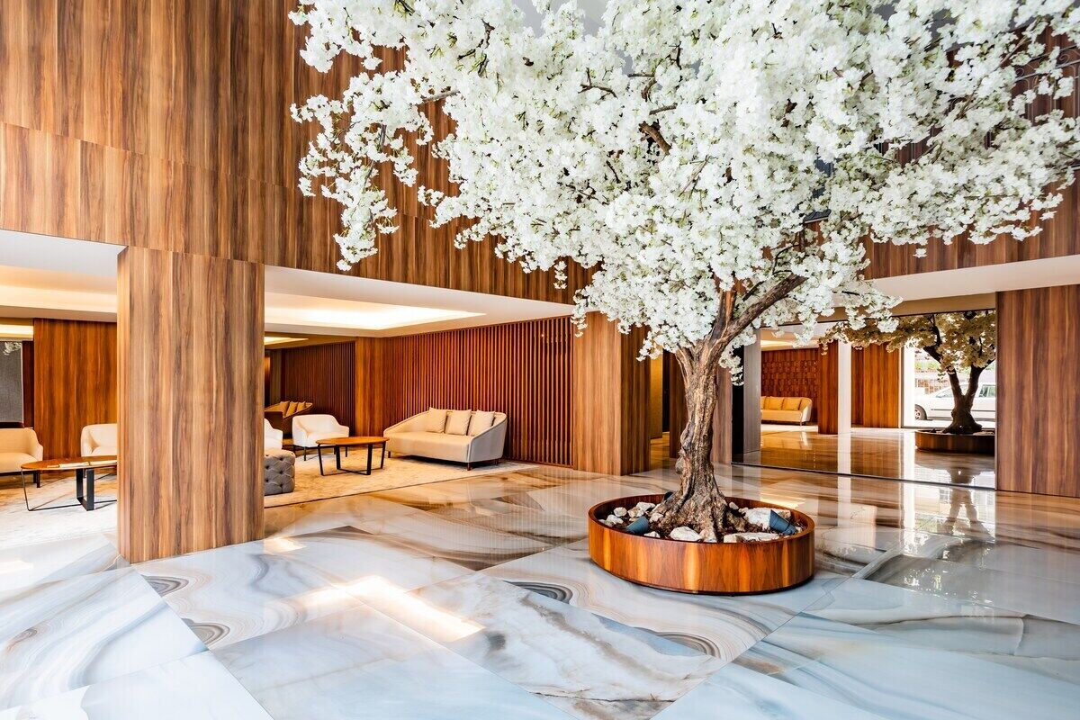 Un vestíbulo moderno con un árbol grande, paneles de madera y suelo de mármol.