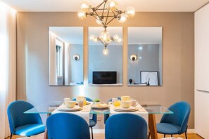 A modern dining area with a glass table, blue chairs, and a chandelier. - Renovato Deluxe Apartment (Porto)