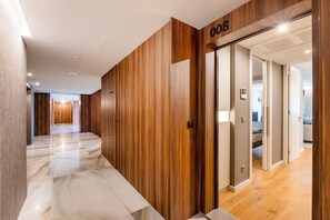 Ein moderner Hotelgang mit Holzvertäfelung, Marmorboden und einer Tür mit der Aufschrift '008'.