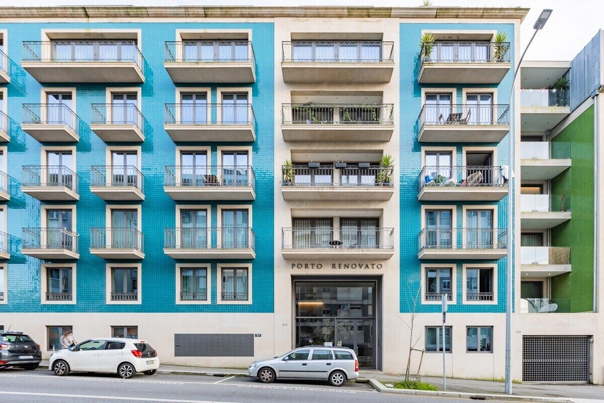 Un edificio de varios pisos con balcones, un escaparate con la leyenda 'PORTO RENOVATO' y coches aparcados en la calle.