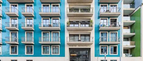 Un edificio de varios pisos con balcones, un escaparate con la leyenda 'PORTO RENOVATO' y coches aparcados en la calle.