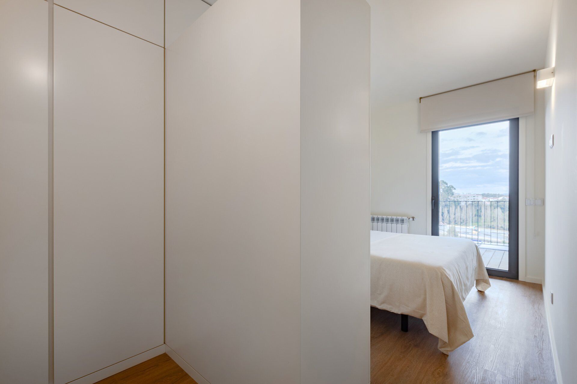 A bedroom with a bed, a radiator, and a large window with a view.
