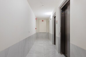 A hallway with a marble floor, white walls, and two doors with emergency exit signs. - Antas Green Executive (Porto)
