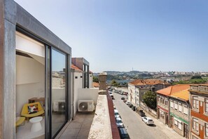 A balcony with a view of a street and buildings, a chair, a small table, and an air conditioning unit. - Duque de Saldanha Duplex Loft (Porto)