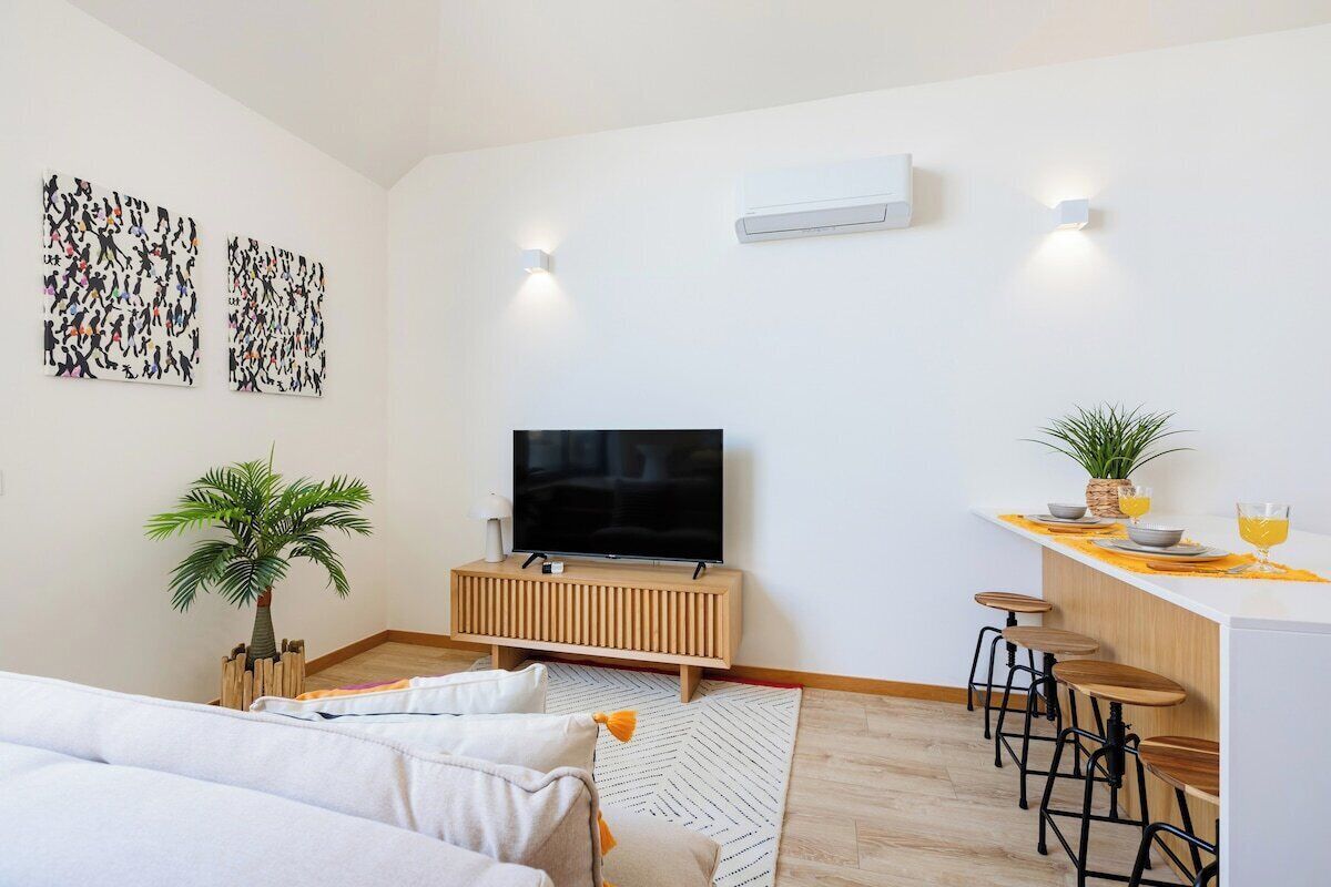 Ein modernes Wohnzimmer mit Fernseher, eine Essecke mit Barhocker und einer Küchenzeile.