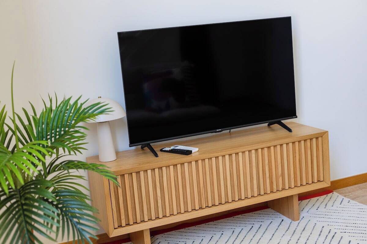 A television on a wooden stand with a remote control, a white lamp, and a potted plant.