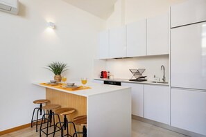A modern kitchen with white cabinets, a wooden island with stools, a coffee machine, and a sink. - Duque de Saldanha Duplex Loft (Porto)