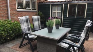 An outdoor patio with a table and chairs, surrounded by greenery and a brick wall. - The Fisherman's Cottage (Egmond aan Zee)