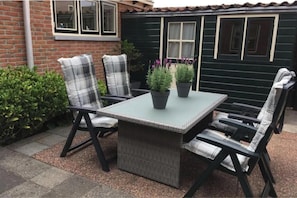 Eine Terrasse im Freien mit Tisch und Stühlen, umgeben von Pflanzen und einer Ziegelmauer.