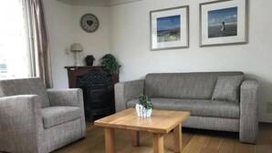 A living room with a grey sofa, two armchairs, a wooden coffee table, and a fireplace. - The Fisherman's Cottage (Egmond aan Zee)